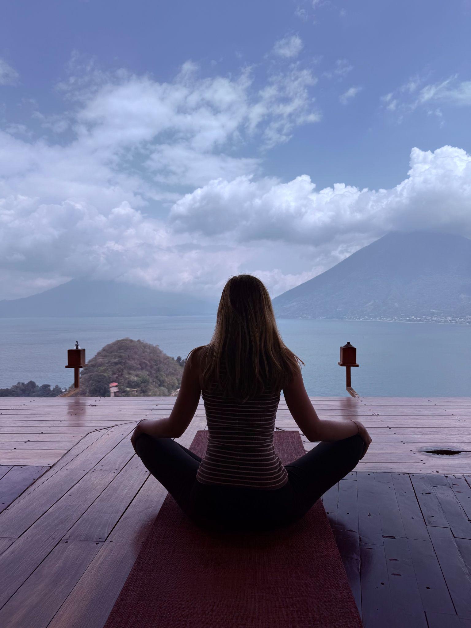 Kadence meditating on a dock overlooking a lake and mountains